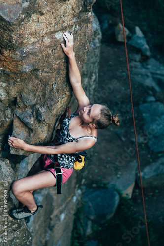 Young strong girl rock climber in a bright T-shirt climbing on a rock.