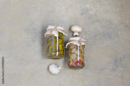 fermented gherkins, cucumbers and champignons in glass jars with spices, bay leaf and garlic on a light background. View from above. Vertical position.