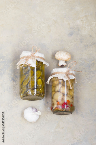 fermented gherkins, cucumbers and champignons in glass jars with spices and garlic on a light background. View from above. Horizontal position.