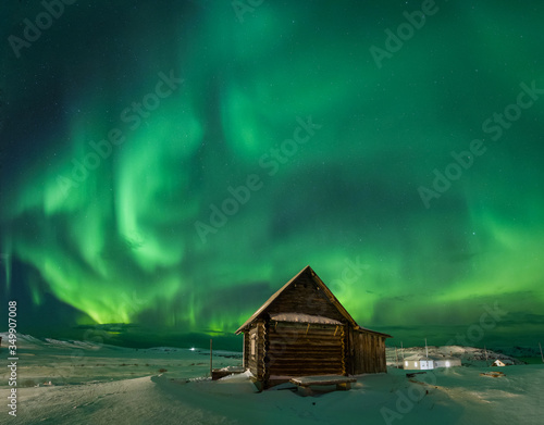 Landscape with northern lights over a wooden house on the coast of the Barents Sea on the Kola Peninsula at night at high ISO sensitivity