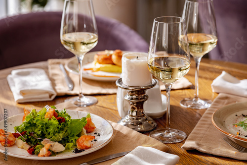 Served table with dishes. On the table are shrimp salad, olivier salad, mashed potatoes with meatballs and an English breakfast. White wine is served for the meal.