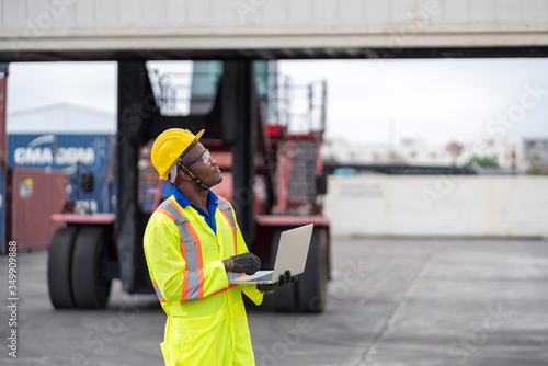 African technician dock worker in protective safety jumpsuit uniform and with hardhat and use digital tablet at cargo container shipping warehouse. transportation import,export logistic industrial