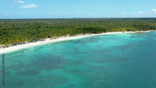Aerial drone zoom in fly over coast line ocean shore during sunny day. Azure turquoise ocean and coastline of palm trees jungle under bright cloudy blue sky
