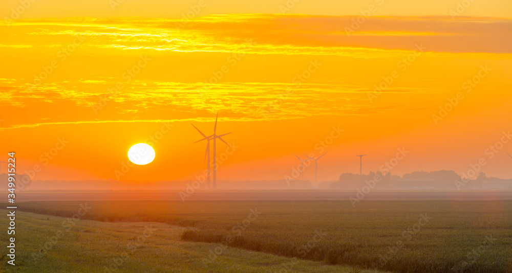 Foggy agricultural field below a misty blue yellow sky in sunlight at a misty sunrise in a spring morning