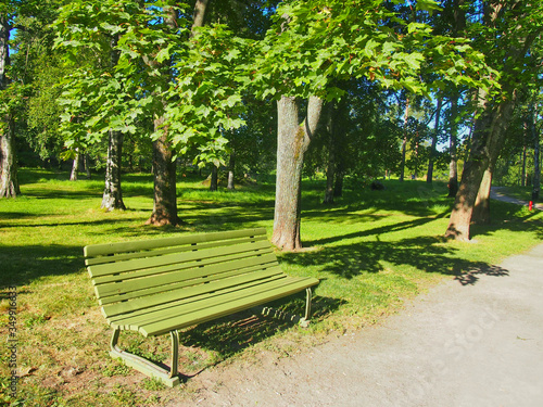 A green chair in the middle of a park walkway with green trees background
