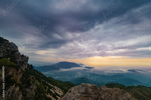 A cloudy sunrise seen from the Venetian mountains called Piccole Dolomiti. The lower clouds cover the plain, only the tops of the hills are visible. The line of light on the horizon. Vicenza, Italy.
