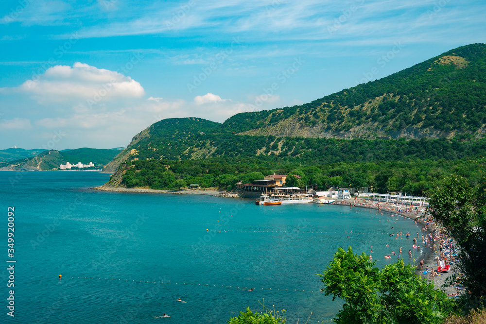 Beautiful coast of the Black Sea with a crowd of tourists on a background of green hills. Sea coastline on a background of green mountains