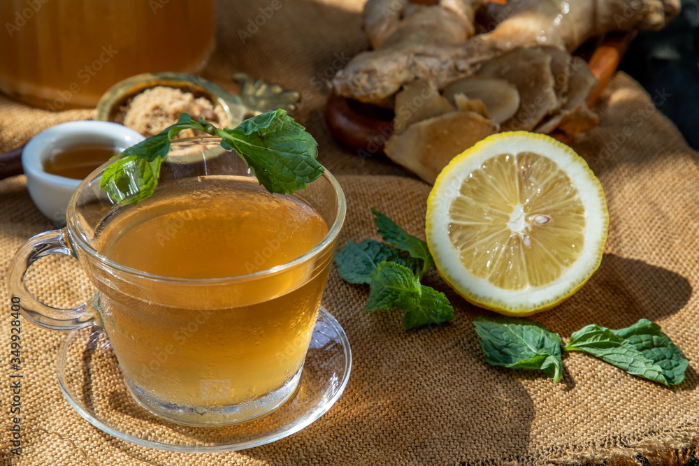 Hot Ginger juice with lemon and mint, root and slices of ginger Served with brown sugar and honey on sackcloth background. Hot Ginger juice with lemon and mint, root and slices of ginger Served with brown sugar and honey on sackcloth background.