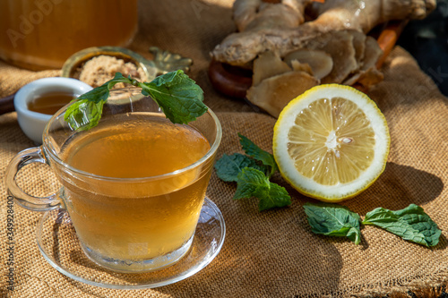 Hot Ginger juice with lemon and mint, root and slices of ginger Served with brown sugar and honey on sackcloth background.