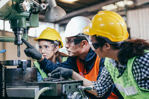 Photography Asian male foreman manager showing case study of factory machine to two engineer trainee young woman in protective uniform