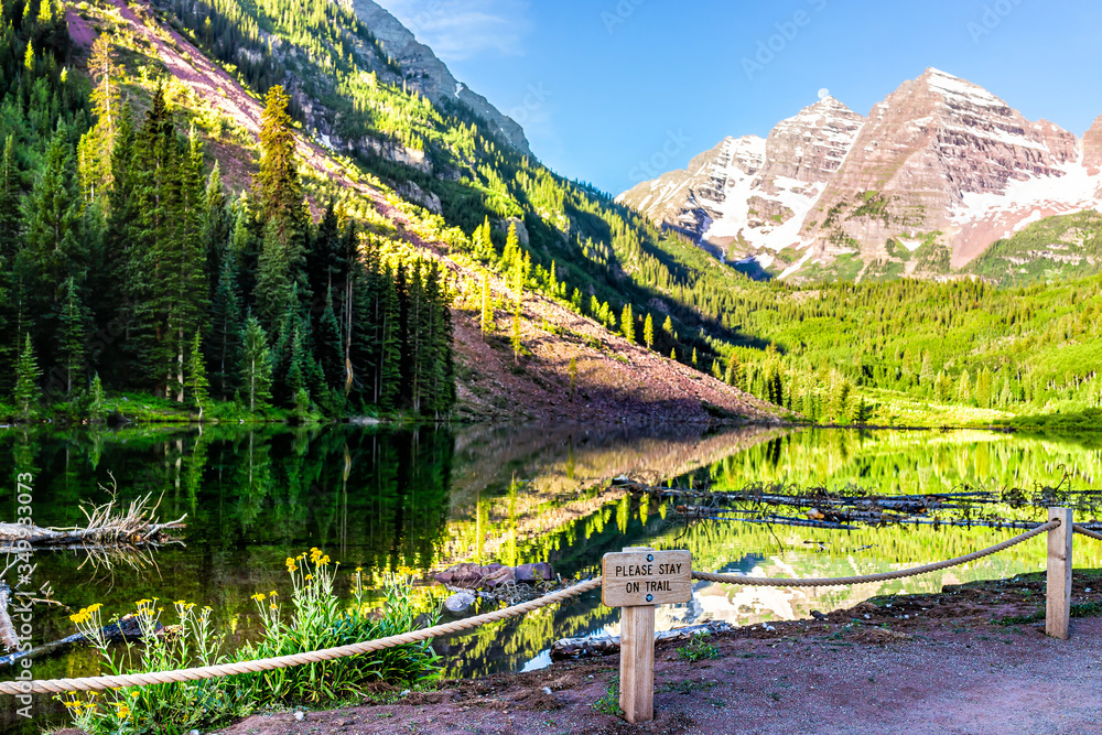 Maroon Bells lake at sunrise view in Aspen, Colorado with rocky mountain peak in July 2019 summer and reflection with sign to stay on trail on fence
