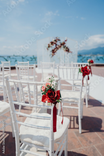 Wedding ceremony registration on a background of the sea, white chairs, red decorations flowers