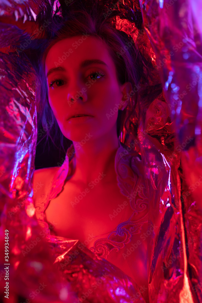 Studio portrait of a beautiful sexy girl model girl in red studio light, abstract background of shiny red foil Studio portrait of a beautiful sexy girl model girl in red studio light, abstract background of shiny red foil