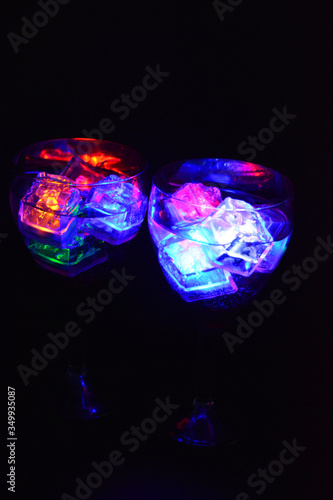 Large glasses with different colors of luminous ice cubes with a tasty drink are located on a black matte background.
