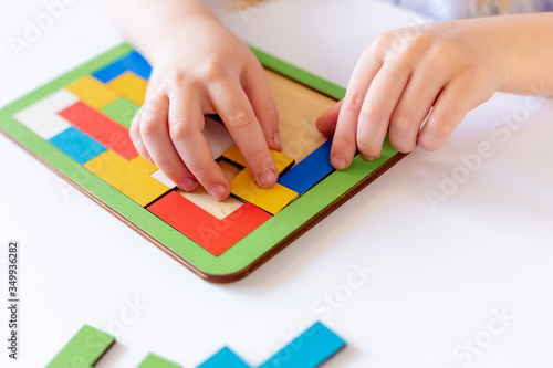 The child collects a puzzle, a constructor of colored parts, and Tetris. Large hands. The process of building the constructor. On light background