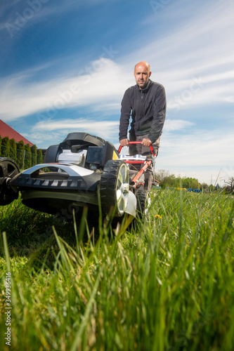 Man mowing, cutting grass on his huge garden yard, green field by the motor garden mower, gardening concept