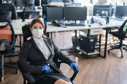 Female manager is sitting in a chair at the workplace. Business woman in mask and gloves at the desk in the office. Concept of work during a virus epidemic.