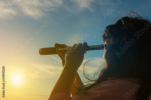 Tableau sur toile Girl looks in a monocular telescope on a sunset background
