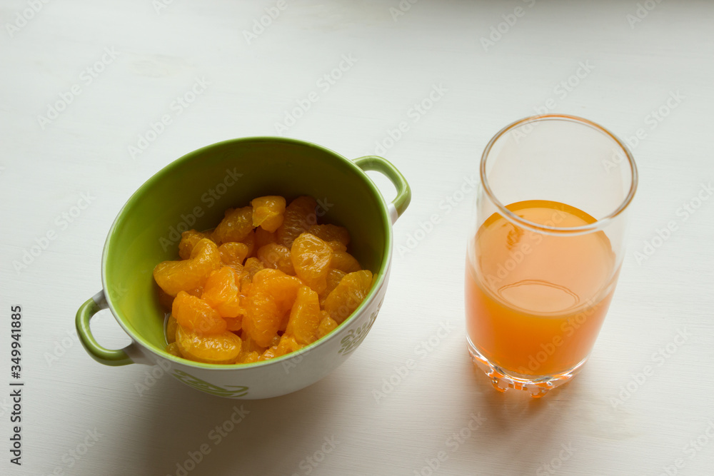 Canned tangerines in sweet sugar syrup are in a deep bowl, next to a glass of tangerine juice. Canned tangerines in sweet sugar syrup are in a deep bowl, next to a glass of tangerine juice.