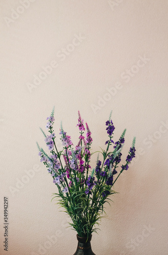 Artificial multi-colored flowers in the form of decor stand in a brown antique vase of wood and bronze on the background of the wall. Decoration for the interior. Photography, concept.