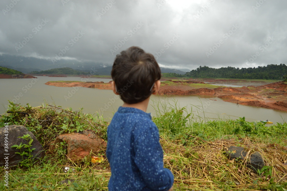 small baby boy kid looking at nature greenery lake sky rains rear view