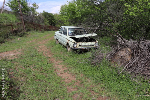 An abandoned car is parked by the road. People drove it and then abandoned it. Now the car is in the woods