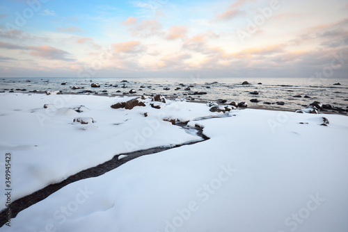 A view of the snow-covered Baltic sea coast at sunset. Stones in the water close-up. Clear blue sky with colorful clouds. Stunning cloudscape. Warm evening light. Idyllic winter scene. Kaltene, Latvia photo