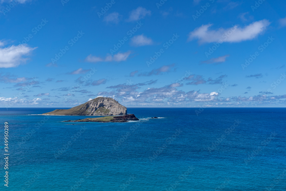 island in the ocean outside of Oahu, Hawaii with blue sky and clouds