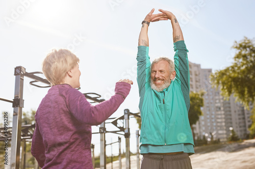 Healthy lifestyle. Beautiful senior or mature family couple in sportswear doing stretching exercises together in the early morning at outdoor gym