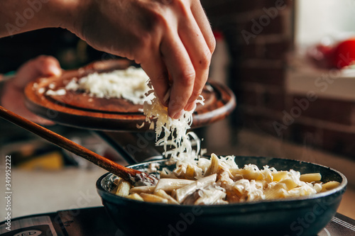 Female hand sprinkles grated cheese on a pan with pasta photo