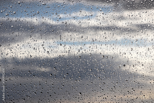 Raindrops on the window glass on blurred background of cloudy sky. Beautiful water drops, rainy weather in town