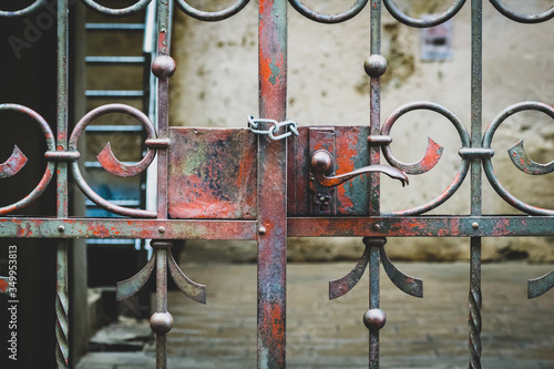 the old iron gate is locked with a metal chain. Close up of a slatted door to an empty courtyard.