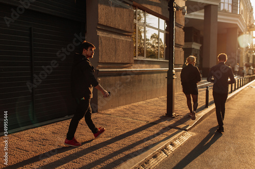 Happy smiling young man using modern smart phone while standing at crosswalk at the sunset in city center