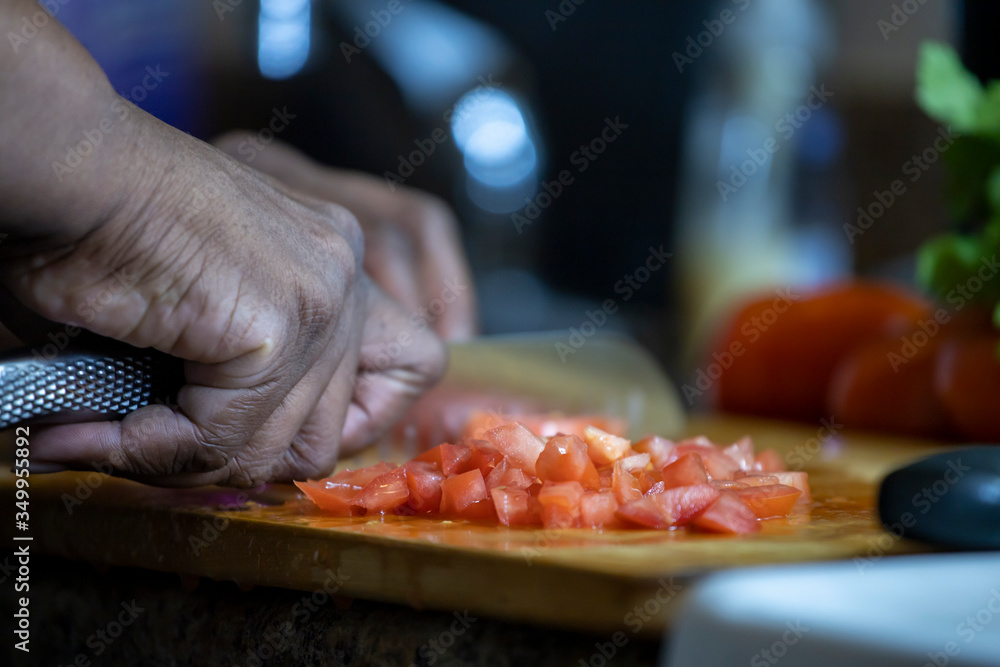 close up view African american woman hand cutting tomatoes into thin slices for healthy and nutritious meal lifestyle. the organic meal the culinary chef is making is delicious
