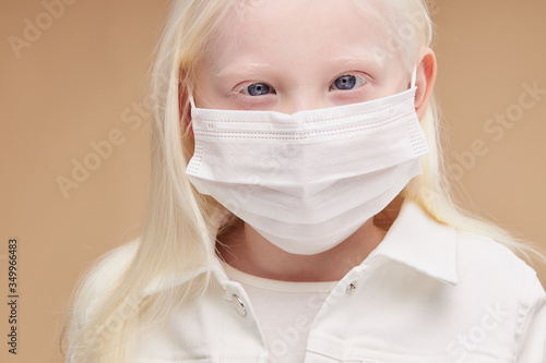 coronavirus, covid-19 concept. little unusual albino child in medical mask isolated, sick kid suffer from emidemic covid-19, protect herself with the use of mask photo