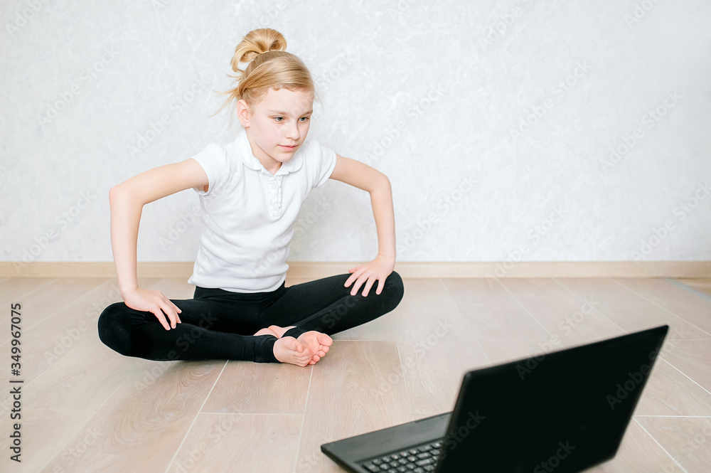 Pretty young girl in sportswear watching online video on laptop and doing fitness exercises at home. Distant training with personal trainer, social distance or self-isolation, online education concept Pretty young girl in sportswear watching online video on laptop and doing fitness exercises at home. Distant training with personal trainer, social distance or self-isolation, online education concept