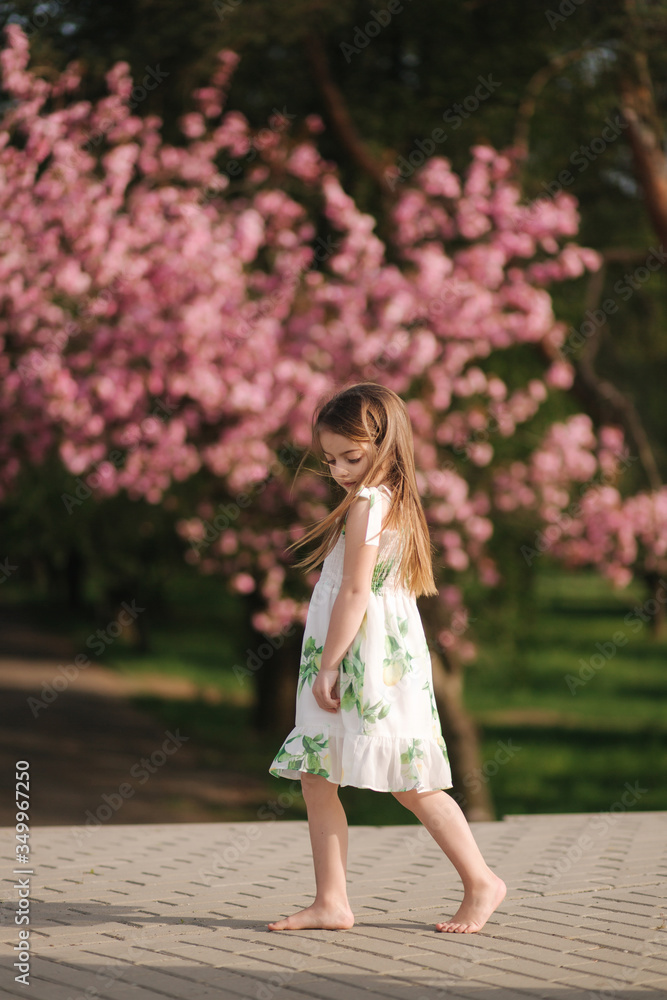 Happy female kid walking barefoot in the park, background of pink sakura tree. End of quarantine. Cute little girl Happy female kid walking barefoot in the park, background of pink sakura tree. End of quarantine. Cute little girl