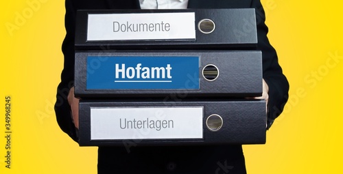 Hofamt. Anwalt im Anzug trägt einen Stapel Ordner. 3 Aktenordner. Blaue Beschriftung mit Text. Hintergrund gelb. Recht, Gesetz, Rechtsprechung photo