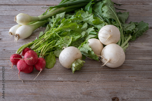 Bunch of white turnips, red radishes and spring onions on wooden table.  Front view of fresh and healty raw vegetables with green leaves