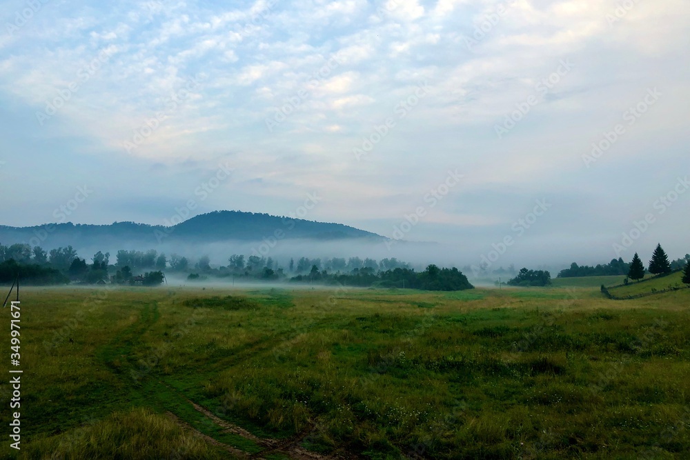 Fototapeta premium Fog in the village at sunrise over the fields and over the mountain