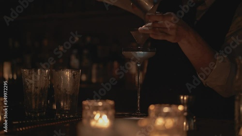 Real time medium shot of a bartender pouring a cocktail into a glass. Bartender prepares cocktails at a bar in Bangkok, Thailand.