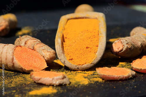 Turmeric powder in a wooden spoon and roots on a dark table (curcuma longa), Kurkuma photo