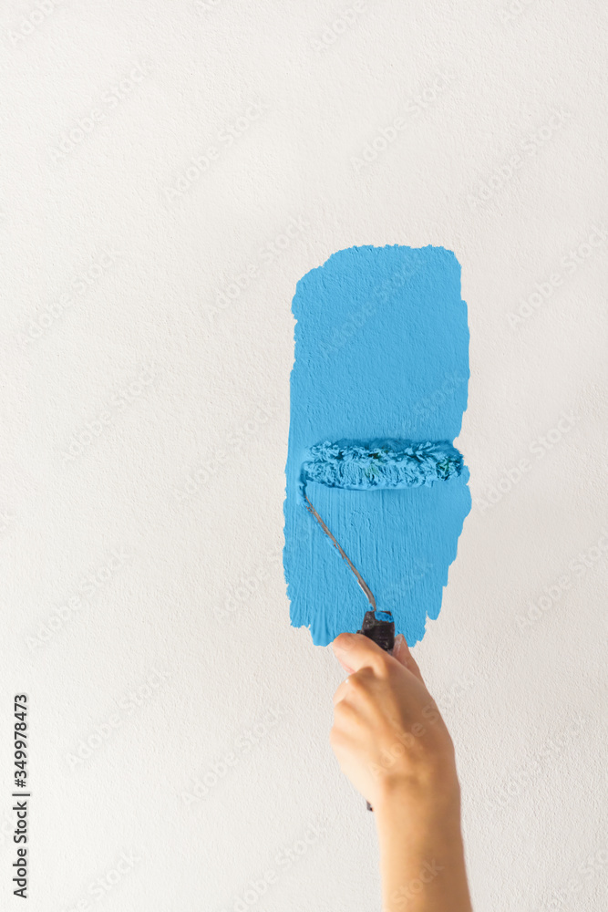 Human hand with a small roller of paint begins to paint a white wall ...