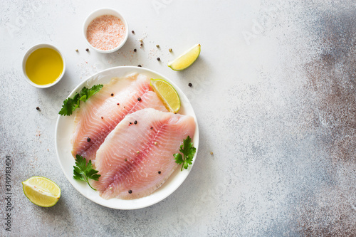 Raw tilapia fillet with lime and spices on a gray stone background