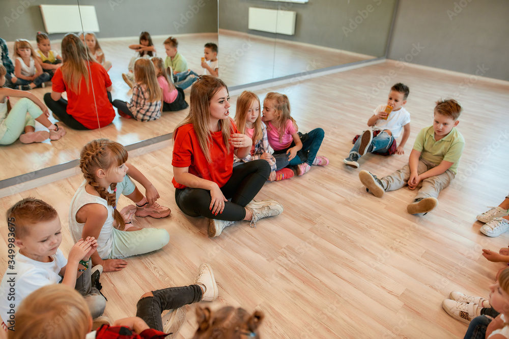 Giving advice. A group of little dancers sitting on the floor gathered around their female dance teacher. Full length portrait of young female dance teacher talking to group of little girls and boys