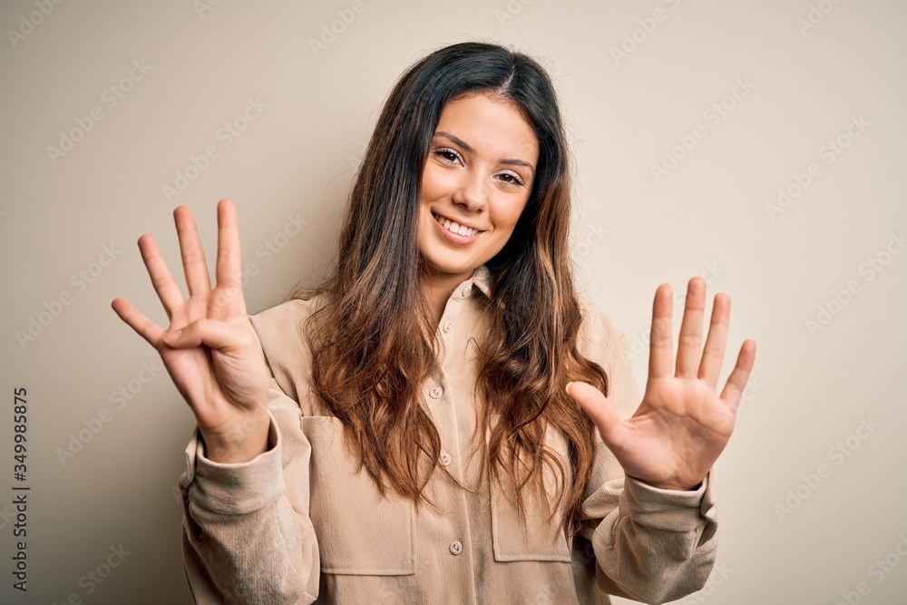 Young beautiful brunette woman wearing casual shirt standing over white background showing and pointing up with fingers number nine while smiling confident and happy. Young beautiful brunette woman wearing casual shirt standing over white background showing and pointing up with fingers number nine while smiling confident and happy.