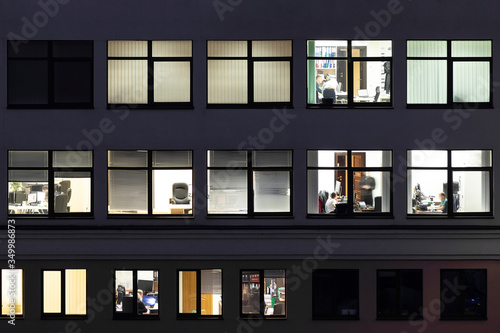 Night aerial view of office or apartment building glass window facade with illuminated lighted workspace rooms. Modern youth business people lifestyle concept