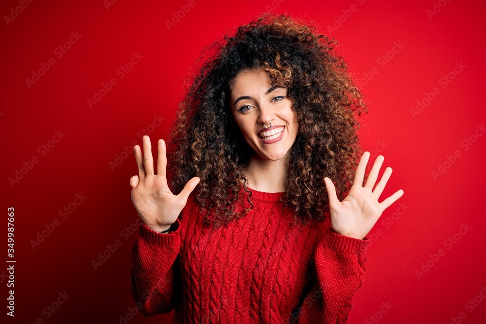 Young beautiful woman with curly hair and piercing wearing casual red sweater showing and pointing up with fingers number nine while smiling confident and happy. Young beautiful woman with curly hair and piercing wearing casual red sweater showing and pointing up with fingers number nine while smiling confident and happy.
