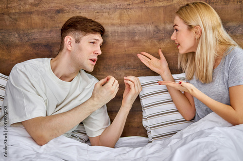 people, relationship difficulties, conflict and family concept - young unhappy caucasian couple having quarrel on bed, they scream, argue, rage out at each other