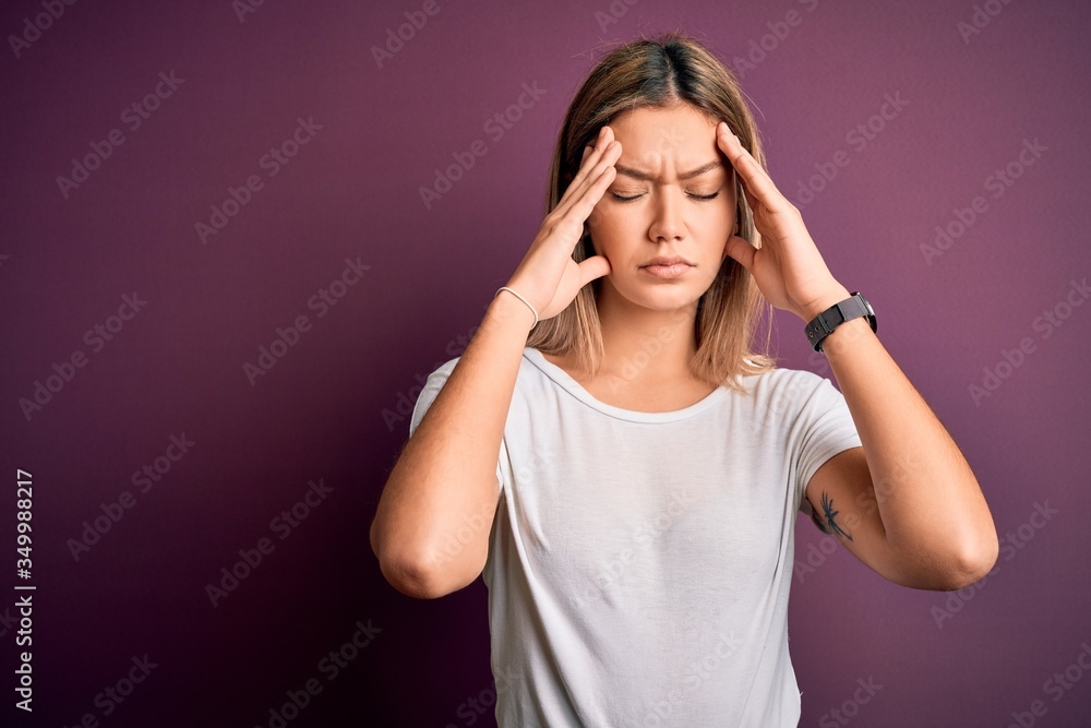 Young beautiful blonde woman wearing casual white t-shirt over purple isolated background suffering from headache desperate and stressed because pain and migraine. Hands on head. Young beautiful blonde woman wearing casual white t-shirt over purple isolated background suffering from headache desperate and stressed because pain and migraine. Hands on head.